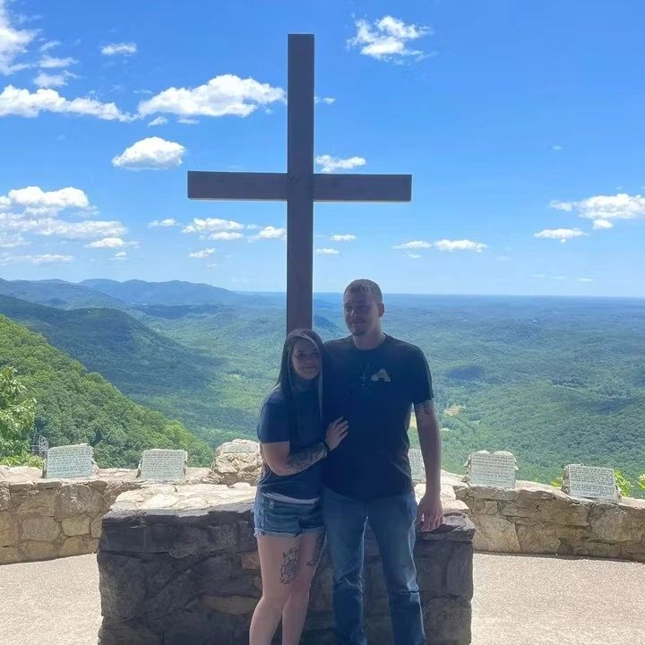 Amanda Foster y su pareja frente a una gran cruz en un mirador